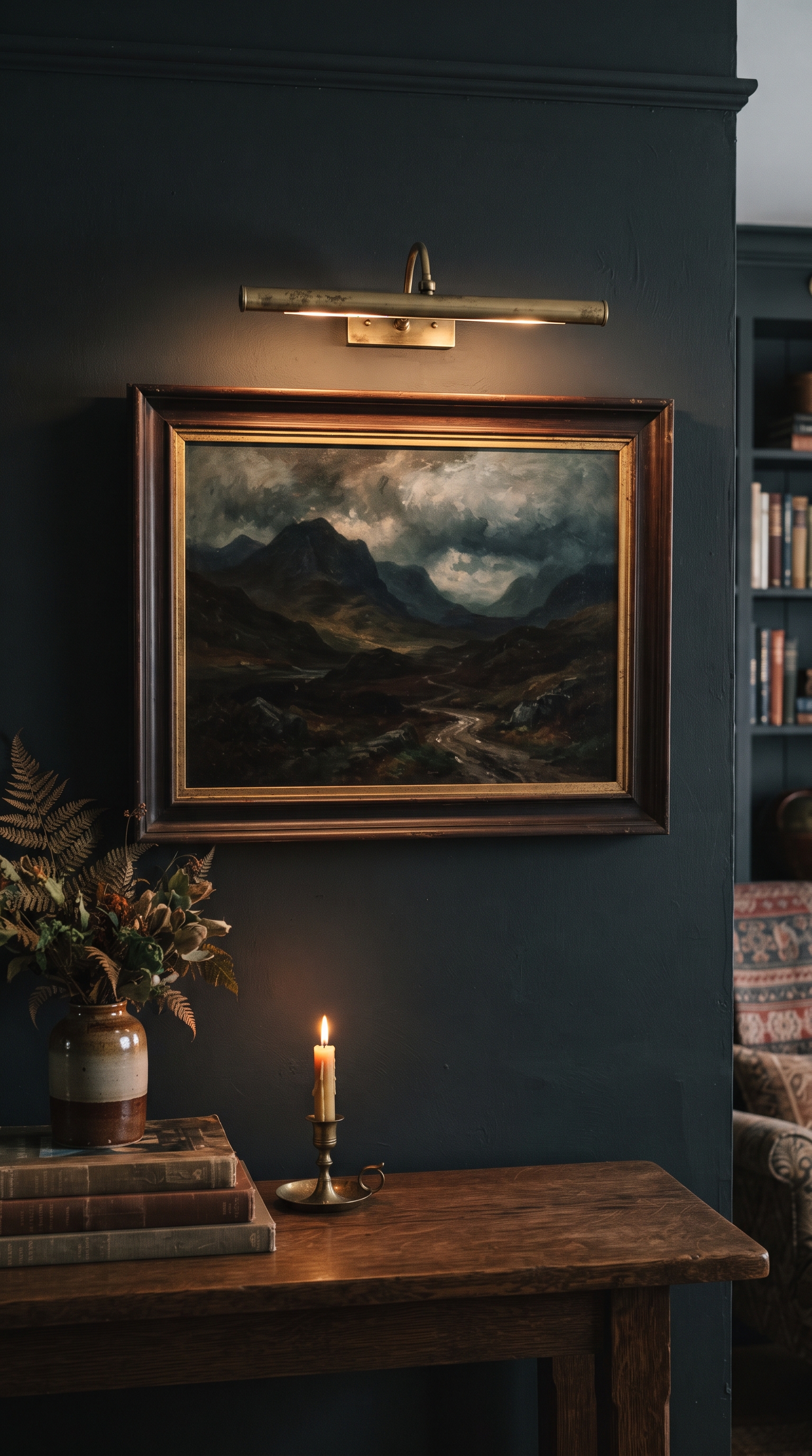 Slim brass picture light washing warm light over a moody landscape oil painting on a charcoal wall