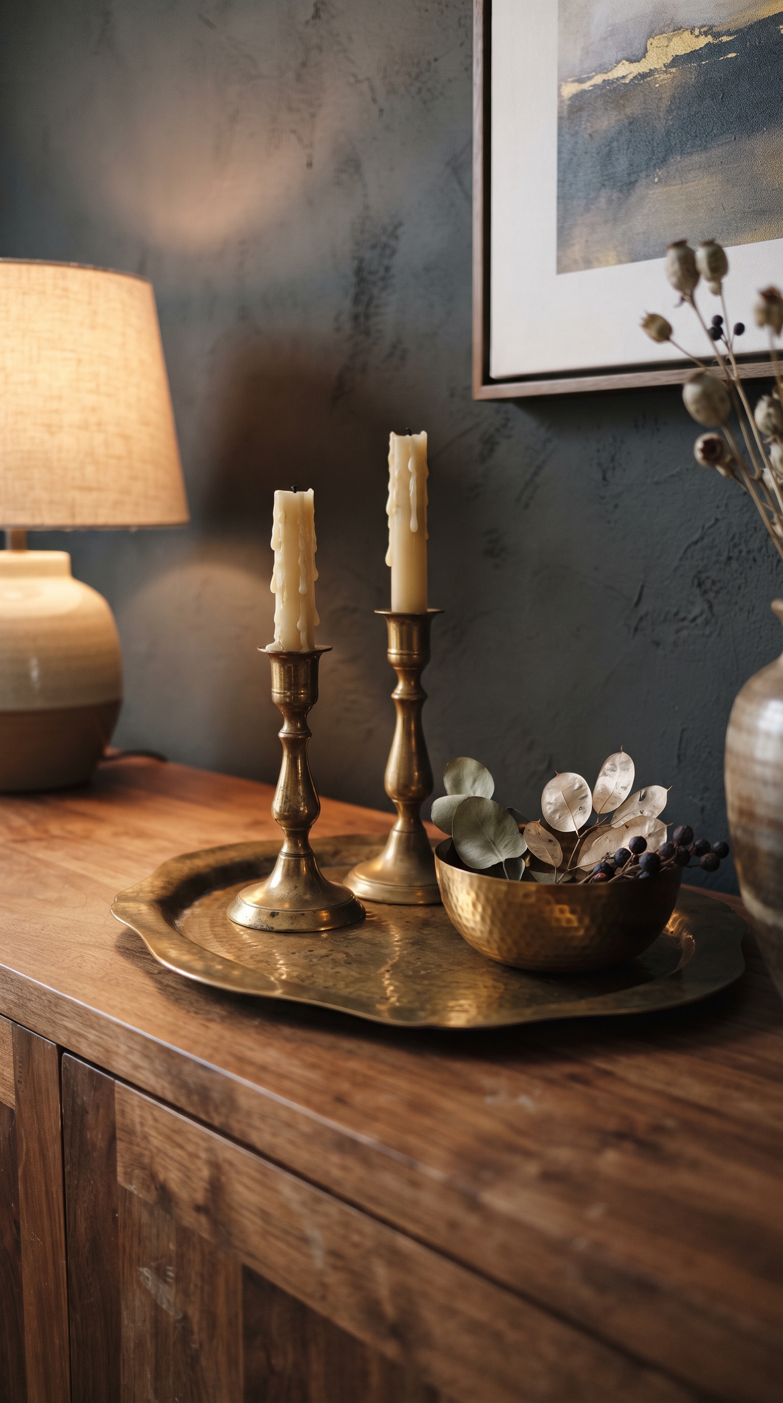 Aged unlacquered brass tray, candlesticks and bowl on a walnut console against a deep charcoal wall